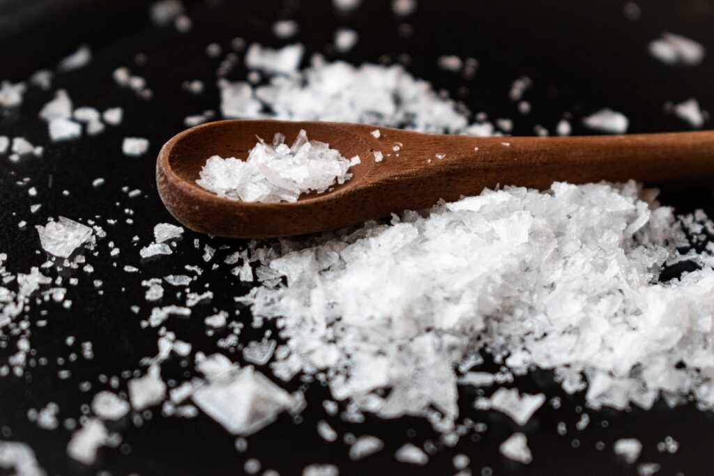 Closeup of wooden spoon arranged with sea salt scattered on table in kitchen