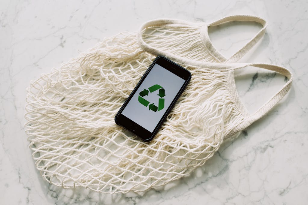 smartphone with simple recycling sign on screen placed on white eco friendly mesh bag 