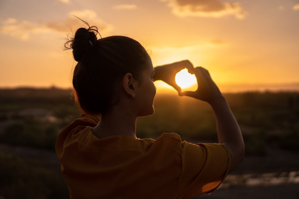 Woman practicing self care, outdoors in sunset doing Hand Heart Sign