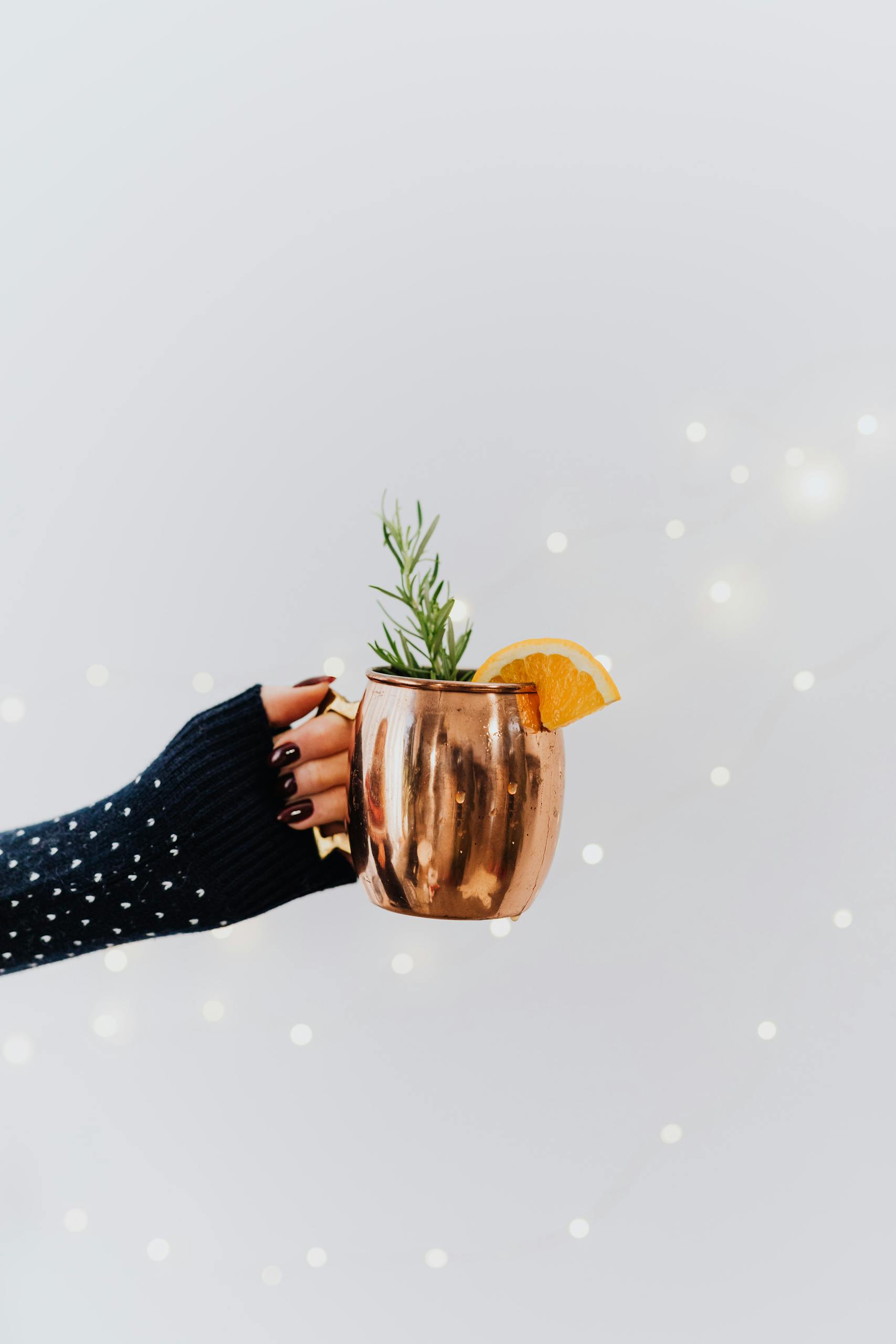 Festive copper mug holding a cocktail garnished with rosemary and orange slice, perfect for winter celebrations.
