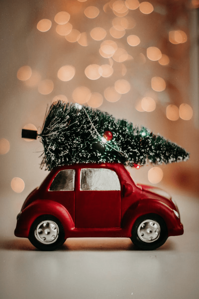 A red toy car carries a cut Christmas tree celebrating holiday traditions